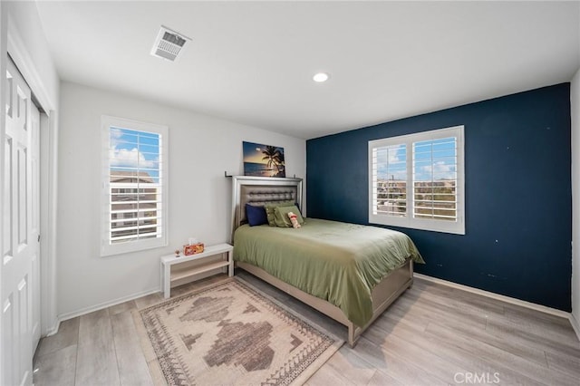 bedroom with baseboards, multiple windows, visible vents, and wood finished floors