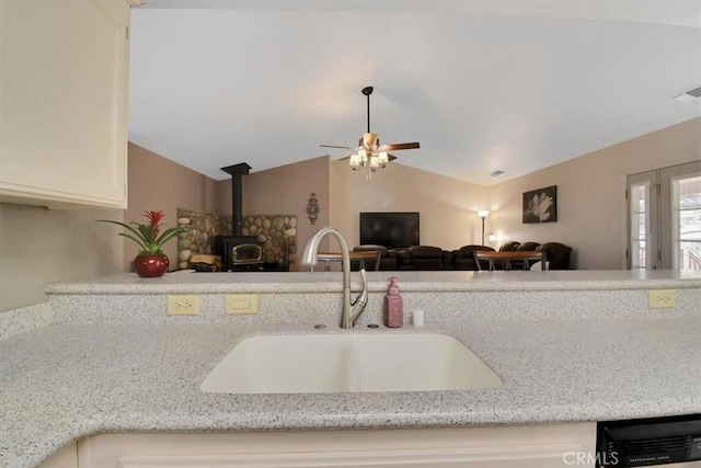 kitchen featuring a sink, open floor plan, light stone countertops, a wood stove, and vaulted ceiling