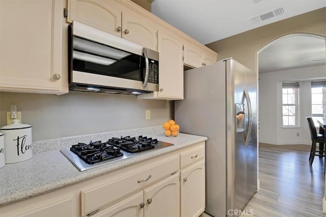kitchen featuring visible vents, arched walkways, appliances with stainless steel finishes, light wood finished floors, and baseboards