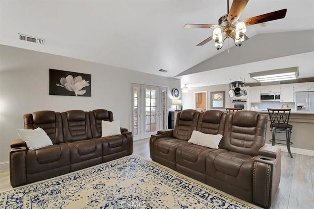 living area with visible vents, a ceiling fan, light wood finished floors, baseboards, and vaulted ceiling