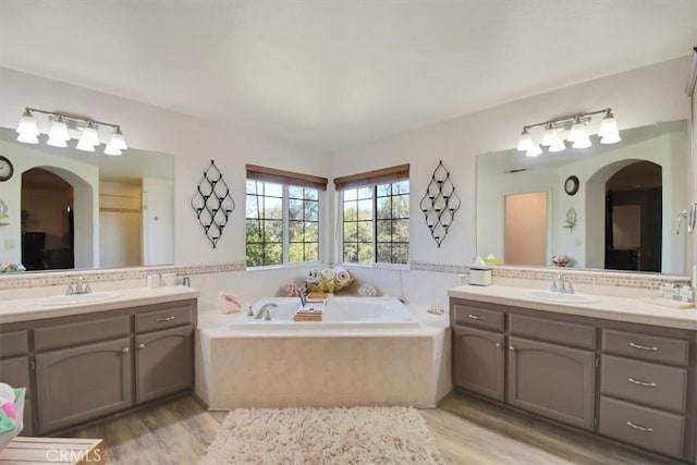 full bathroom with two vanities, a bath, and a sink