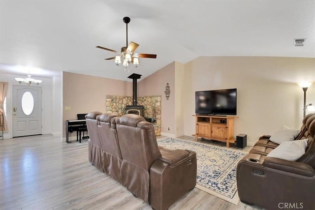 living room featuring visible vents, light wood-style flooring, baseboards, lofted ceiling, and a wood stove