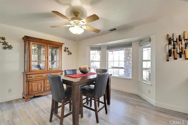 dining space with a ceiling fan, baseboards, visible vents, and light wood finished floors