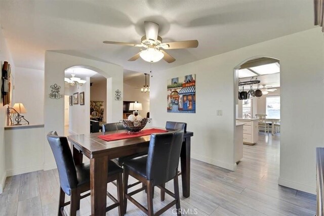 dining space featuring baseboards, arched walkways, light wood-style floors, and ceiling fan
