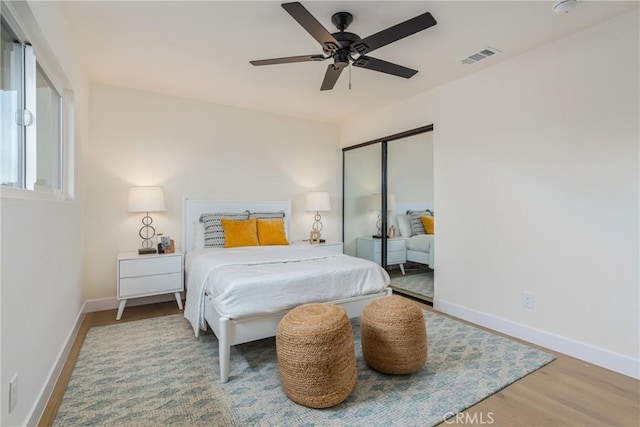 bedroom featuring a ceiling fan, visible vents, baseboards, and wood finished floors