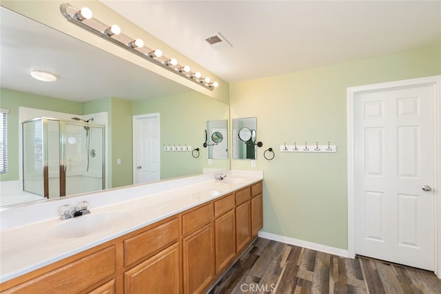 full bathroom featuring visible vents, a shower stall, double vanity, wood finished floors, and a sink