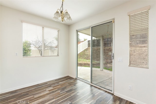 spare room featuring dark wood finished floors, a notable chandelier, and baseboards