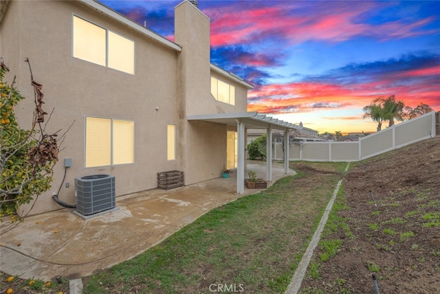 back of house at dusk with stucco siding, cooling unit, a patio area, and a fenced backyard