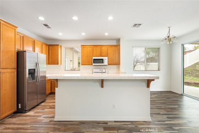 kitchen featuring visible vents, an island with sink, stainless steel refrigerator with ice dispenser, tile countertops, and white microwave