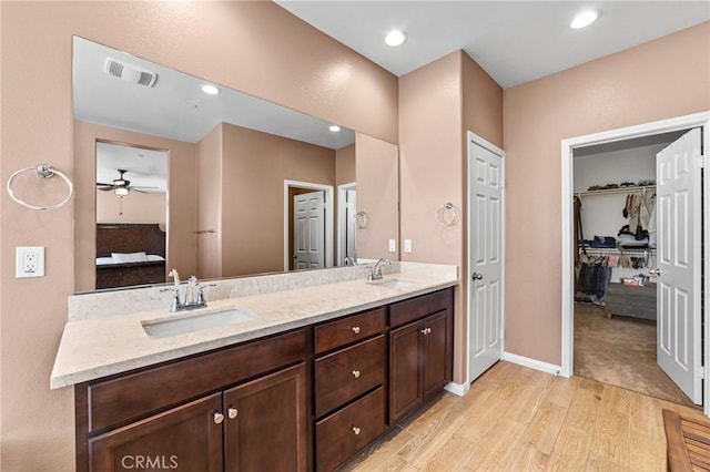 ensuite bathroom with double vanity, ensuite bathroom, a sink, wood finished floors, and baseboards