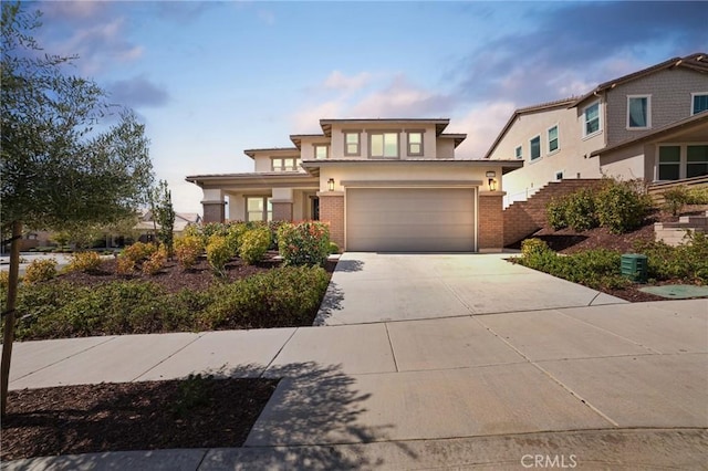 view of front facade featuring a garage, brick siding, driveway, and stucco siding