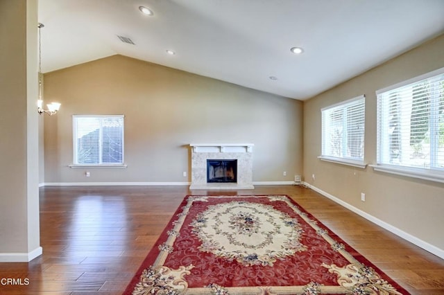 living area with lofted ceiling, visible vents, a premium fireplace, and wood finished floors