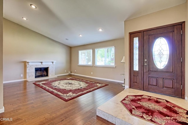 foyer entrance with lofted ceiling, recessed lighting, wood finished floors, a high end fireplace, and baseboards