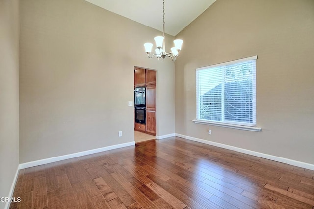 empty room with dark wood-type flooring, a notable chandelier, high vaulted ceiling, and baseboards