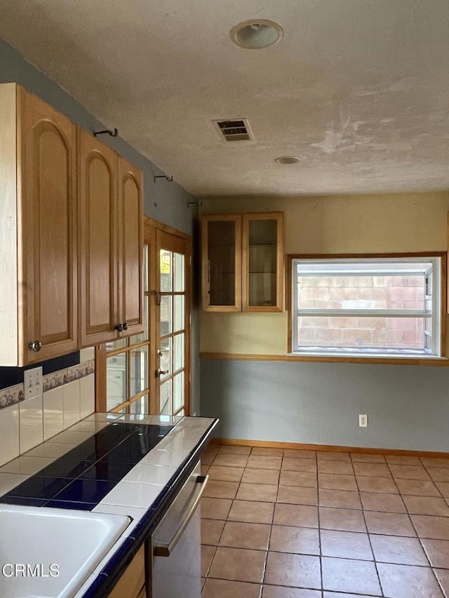 kitchen featuring tile countertops, stainless steel dishwasher, visible vents, and baseboards