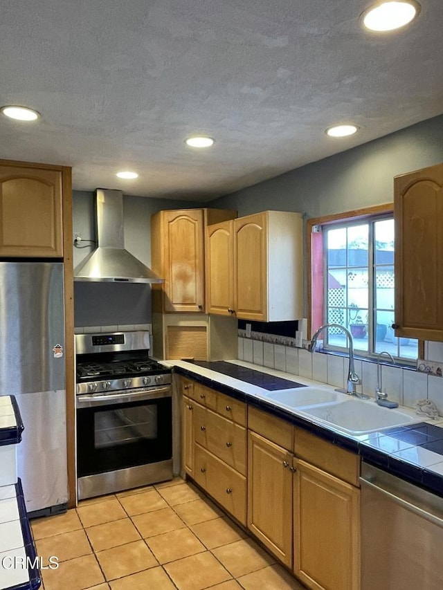 kitchen featuring recessed lighting, a sink, appliances with stainless steel finishes, tile counters, and wall chimney exhaust hood