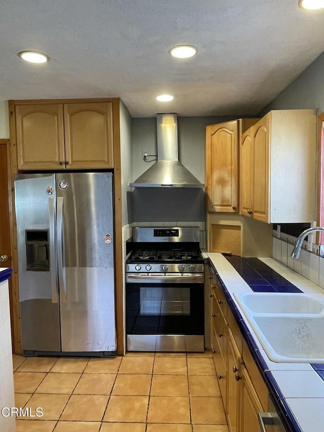 kitchen featuring stainless steel appliances, decorative backsplash, light tile patterned flooring, a sink, and wall chimney range hood