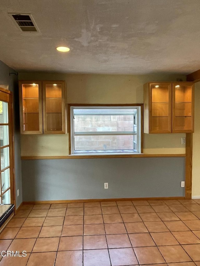 kitchen with light tile patterned flooring, recessed lighting, visible vents, baseboards, and glass insert cabinets