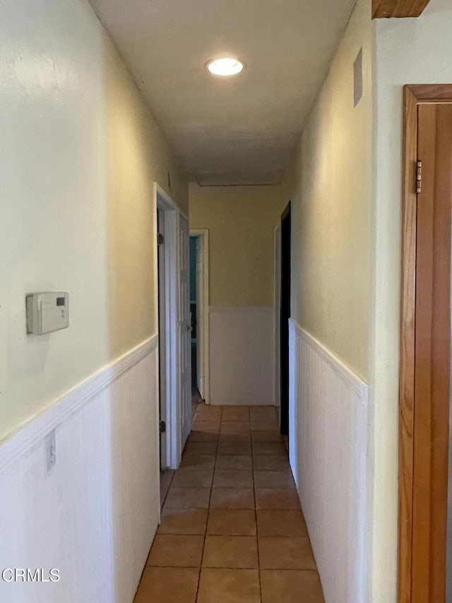 hall featuring a wainscoted wall and light tile patterned flooring