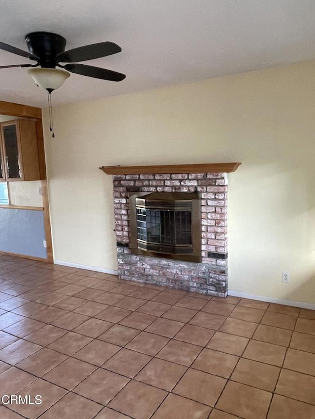 unfurnished living room with a brick fireplace, light tile patterned floors, baseboards, and a ceiling fan