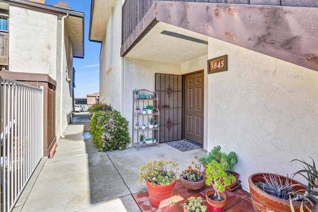 view of exterior entry featuring stucco siding and fence