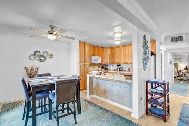 kitchen with white microwave, visible vents, crown molding, light wood-style floors, and stove