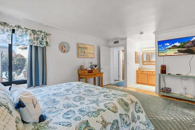 bedroom with ensuite bath, visible vents, wood finished floors, and ornamental molding