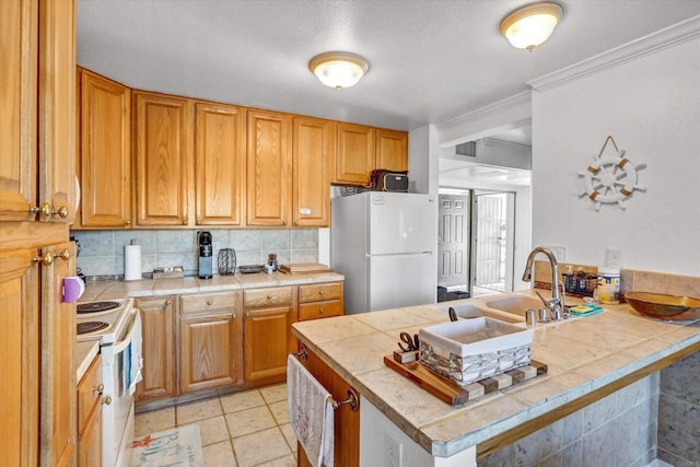 kitchen with white appliances, a peninsula, tile counters, crown molding, and backsplash