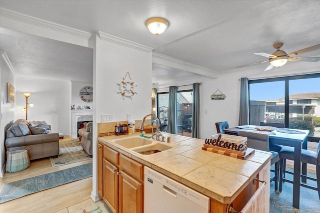 kitchen with open floor plan, dishwasher, a lit fireplace, ornamental molding, and a sink