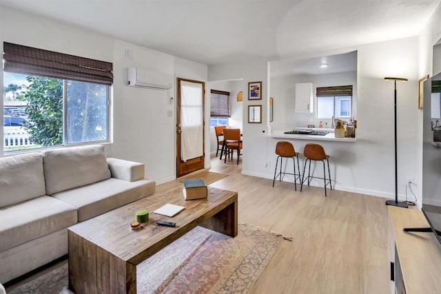 living room with light wood-type flooring, baseboards, and a wall mounted AC