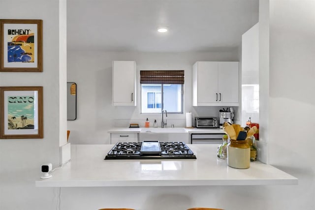 kitchen featuring black gas stovetop, a peninsula, a sink, white cabinets, and light countertops