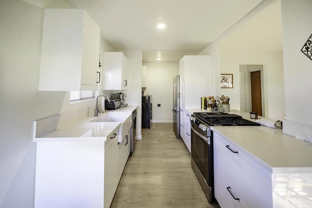 kitchen featuring stainless steel appliances, a sink, white cabinetry, light countertops, and light wood finished floors