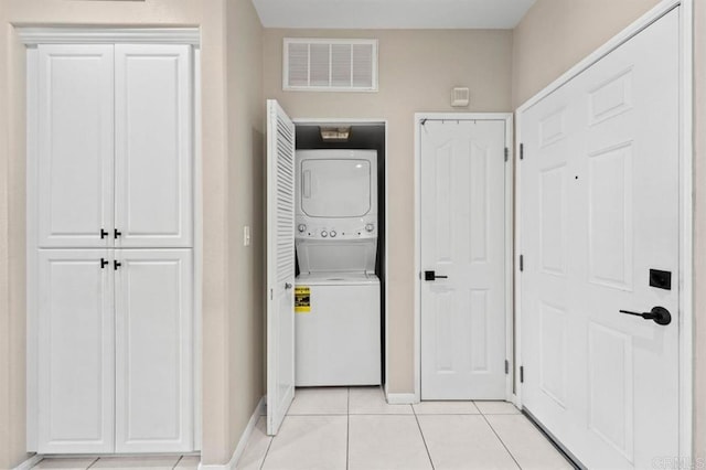 washroom with light tile patterned floors, stacked washer and dryer, visible vents, laundry area, and baseboards