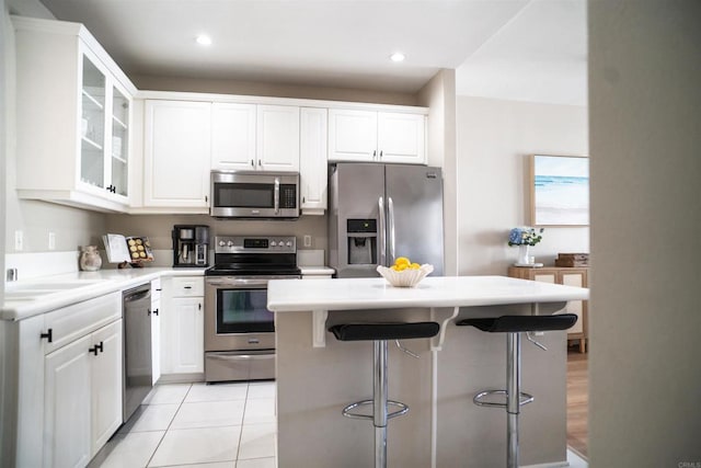 kitchen with light tile patterned floors, stainless steel appliances, glass insert cabinets, white cabinetry, and a kitchen breakfast bar