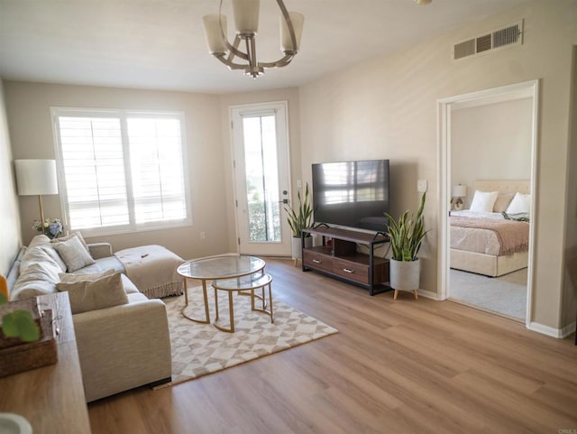 living room featuring a chandelier, visible vents, baseboards, and wood finished floors