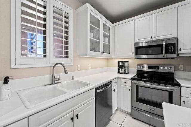 kitchen featuring light tile patterned floors, glass insert cabinets, stainless steel appliances, white cabinetry, and a sink