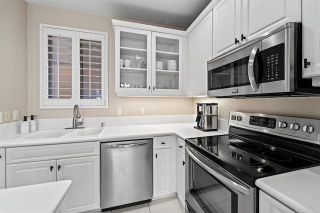 kitchen featuring appliances with stainless steel finishes, white cabinets, a sink, and glass insert cabinets