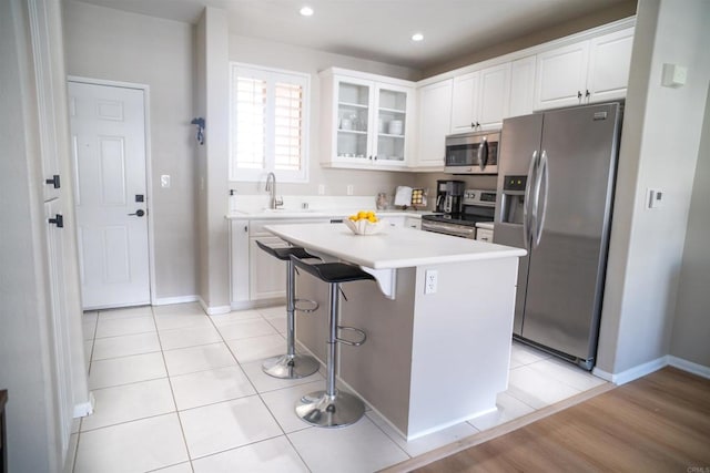 kitchen featuring white cabinetry, appliances with stainless steel finishes, a center island, a kitchen bar, and glass insert cabinets