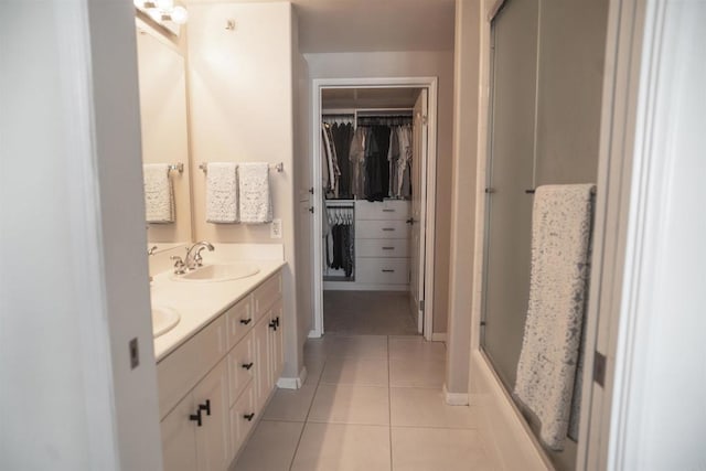 full bathroom with a walk in closet, double vanity, a sink, tile patterned flooring, and baseboards