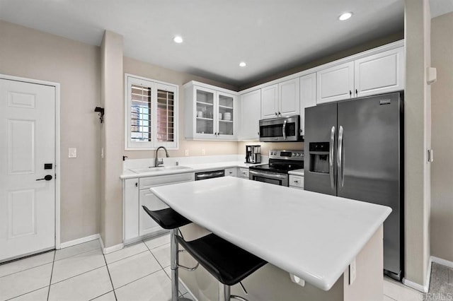 kitchen featuring light tile patterned floors, a sink, white cabinetry, appliances with stainless steel finishes, and glass insert cabinets