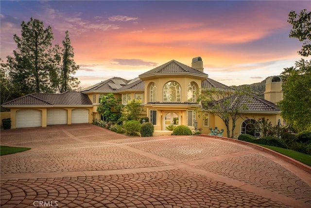 mediterranean / spanish-style house featuring curved driveway, a tiled roof, stucco siding, a chimney, and an attached garage