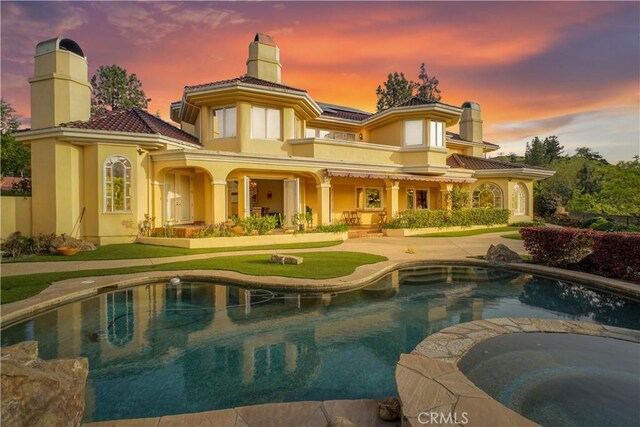 22537 N Summit Ridge Cir, Chatsworth, CA 91311 - back of house at dusk featuring a chimney, stucco siding, a tile roof, and a pool with connected hot tub