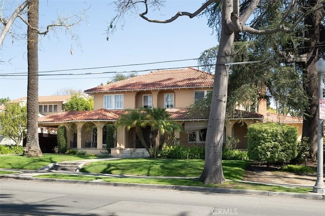 mediterranean / spanish house featuring stucco siding, covered porch, a tiled roof, and a front yard