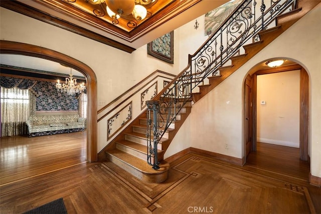 staircase featuring ornamental molding, baseboards, a high ceiling, arched walkways, and a notable chandelier