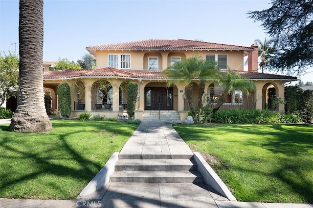 mediterranean / spanish-style home with a tile roof, stucco siding, a front yard, and a porch