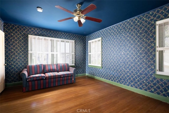 sitting room with baseboards, wallpapered walls, a ceiling fan, and wood finished floors