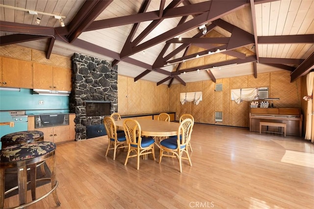 dining space with vaulted ceiling with beams, wood finished floors, wooden ceiling, and a stone fireplace
