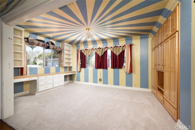 interior space with carpet flooring, crown molding, baseboards, built in desk, and wallpapered walls
