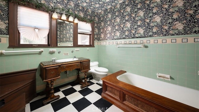 bathroom featuring a wainscoted wall, wallpapered walls, tile patterned floors, toilet, and a tub