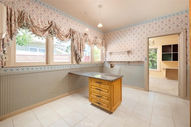 kitchen featuring light tile patterned floors, wallpapered walls, stone counters, and wainscoting